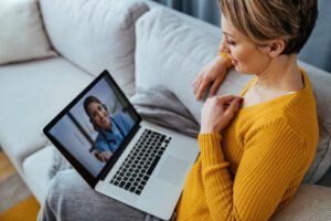 A woman sits at her computer, engaged in a virtual psychology appointment via video conference.